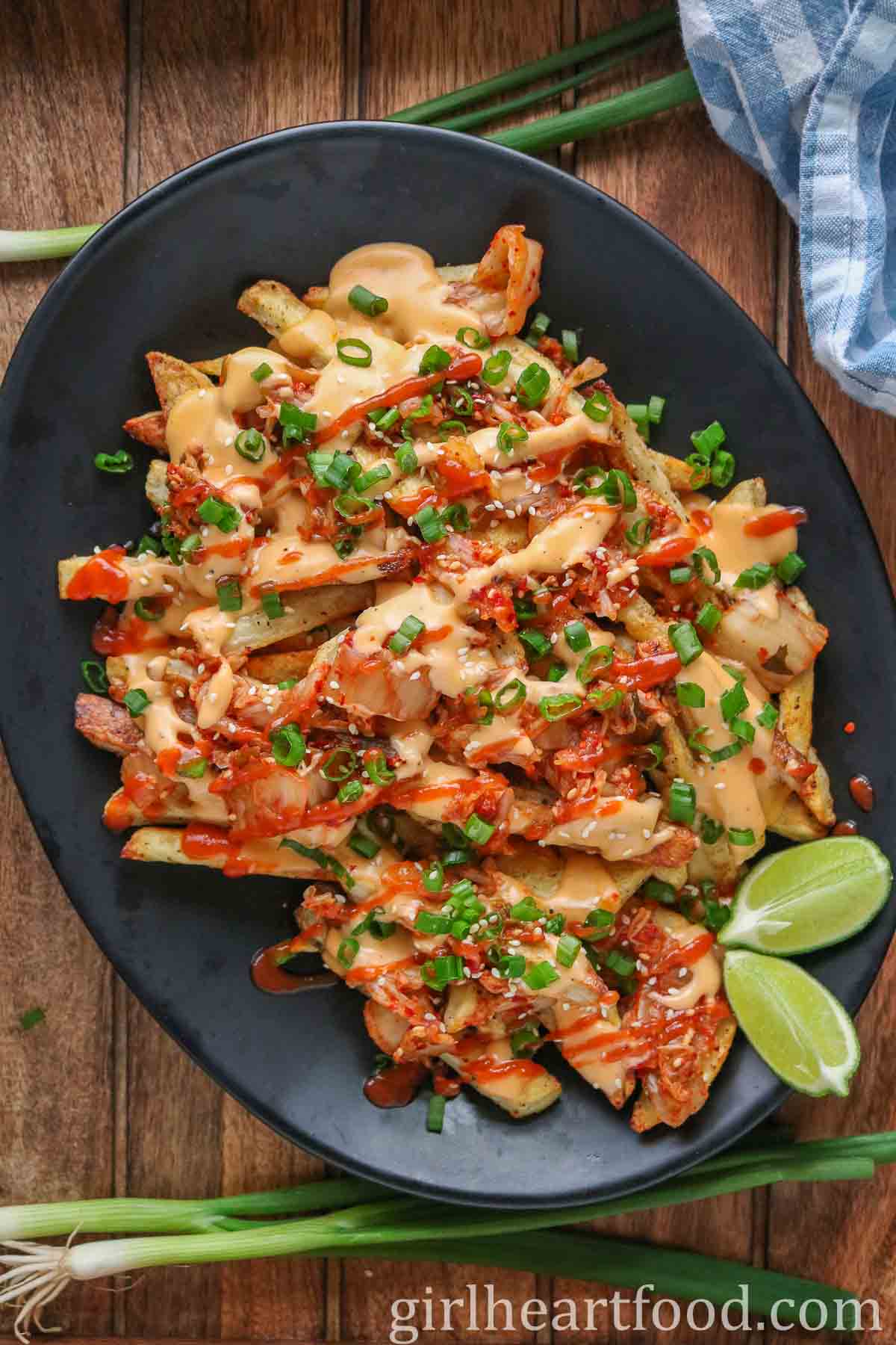 Cheesy kimchi fries and lime wedges on a platter with green onion on either side.