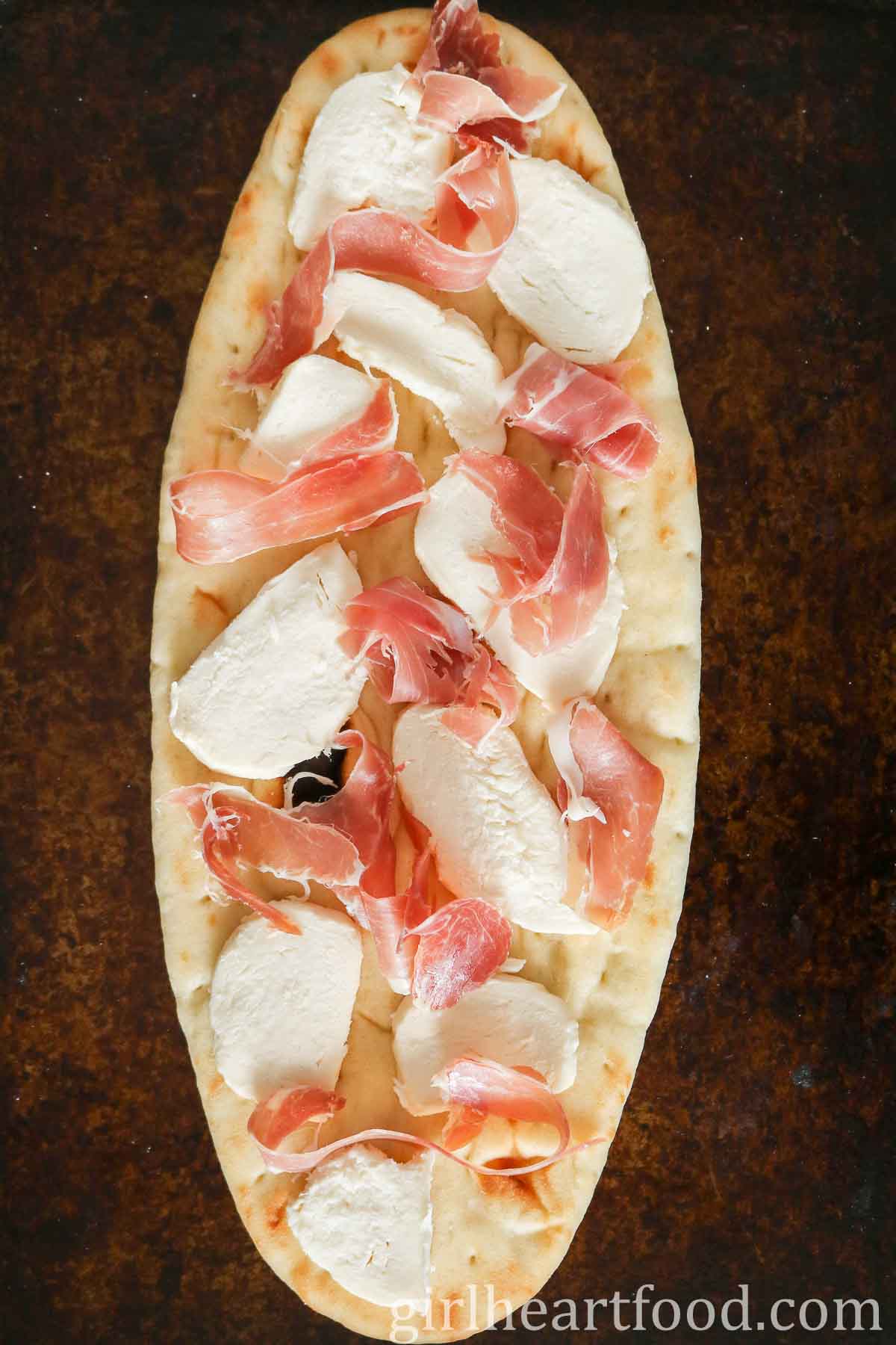 Mozzarella and prosciutto flatbread on a sheet pan before being baked.