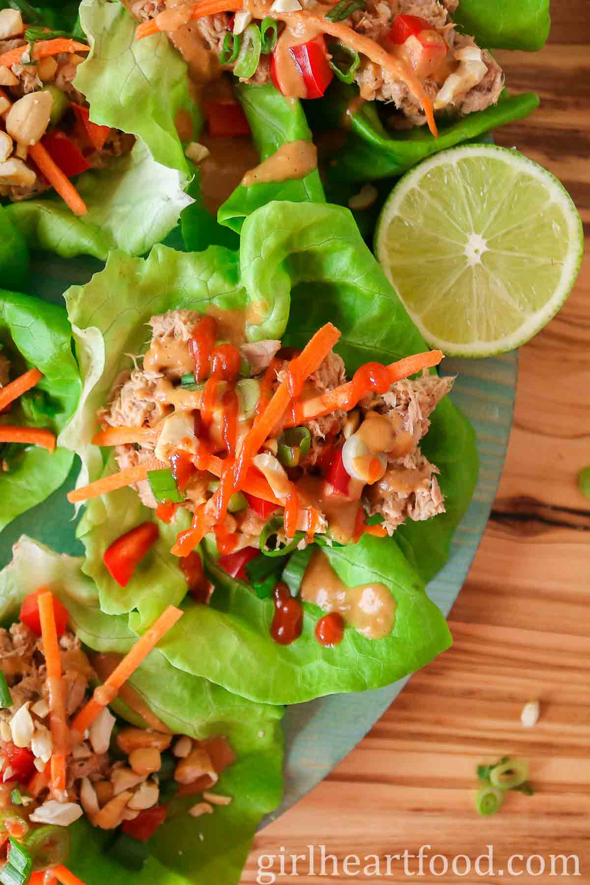 Tuna lettuce wraps with peanut sauce and hot sauce next to half a lime.