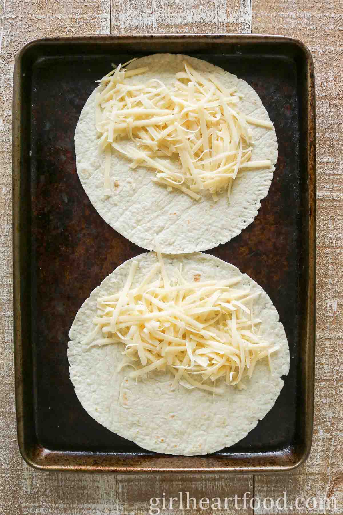 Two tortillas with shredded cheese on a sheet pan.