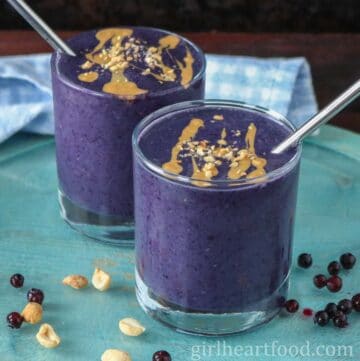 Two glasses of blueberry peanut butter smoothie, one in front of the other.