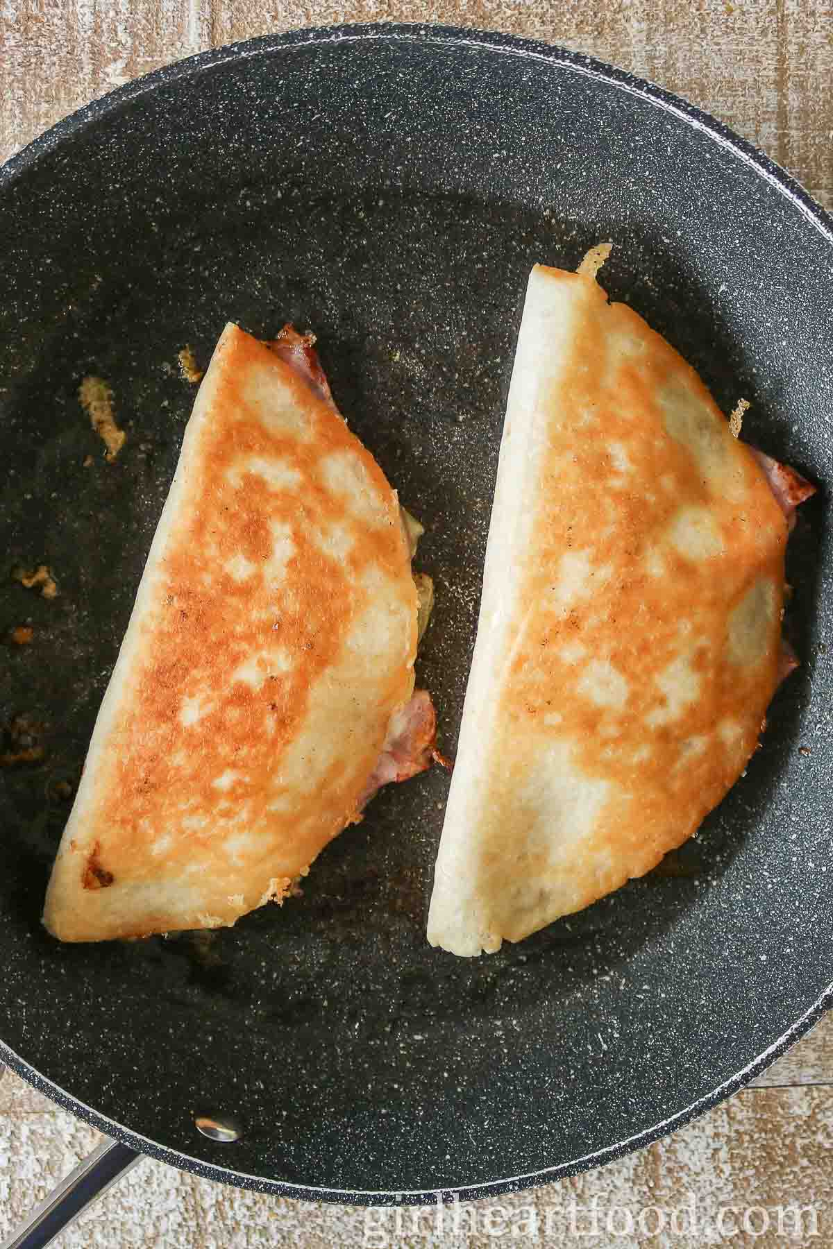 Two crispy quesadillas in a frying pan.