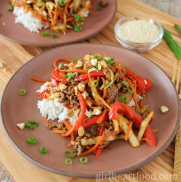 Ground beef stir-fry & rice on a plate, in front of another plate of stir fry & sesame seeds.