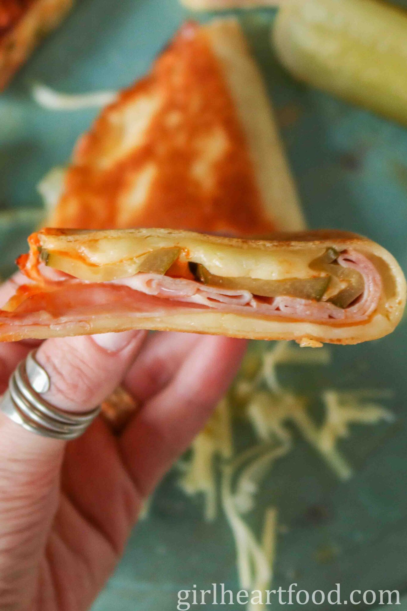 Hand holding a pickle, ham and cheese quesadilla.