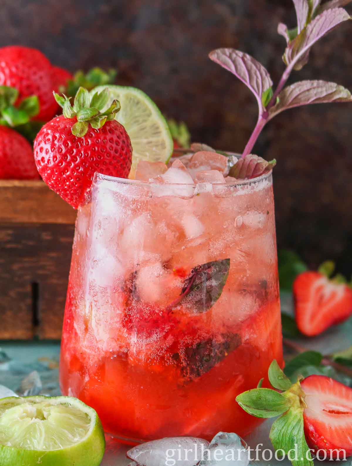 Glass of strawberry mocktail garnished with strawberry, lime and mint.
