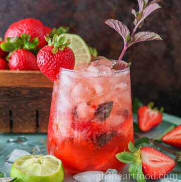 Glass of strawberry mocktail in front of a basket of strawberries.