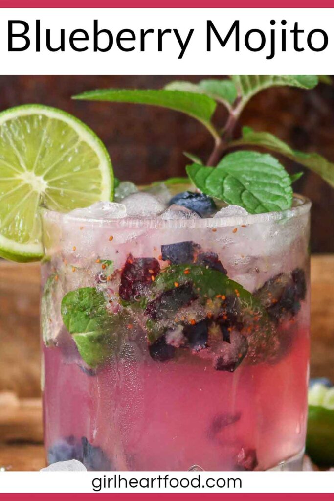 Glass of blueberry mojito garnished with mint, lime and berries.