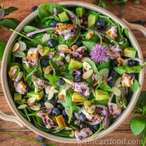 Blueberry spinach salad in a serving bowl drizzled with vinaigrette.