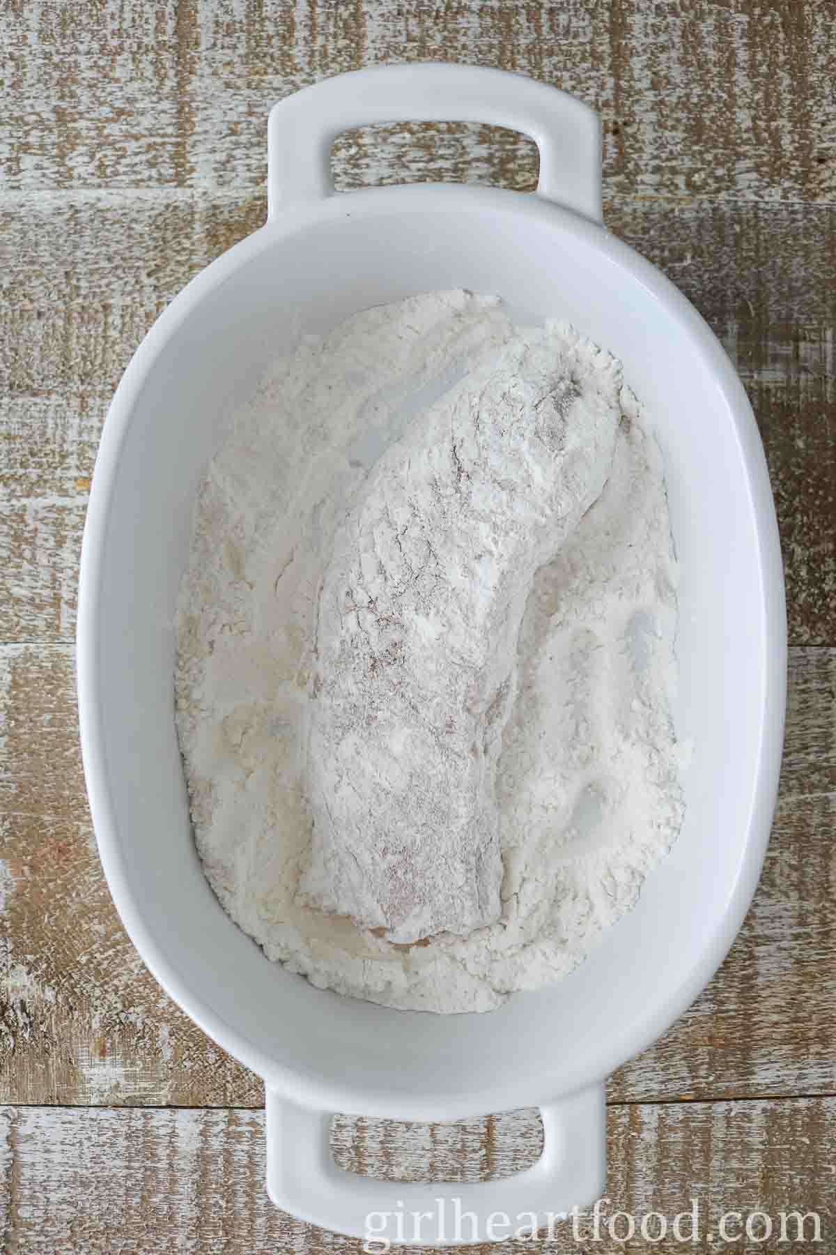 Flour-coated cod fillet in a white dish.
