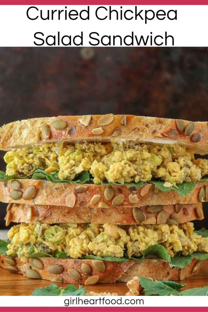 Close-up of a stack of two chickpea salad sandwiches next to baby kale and walnuts.