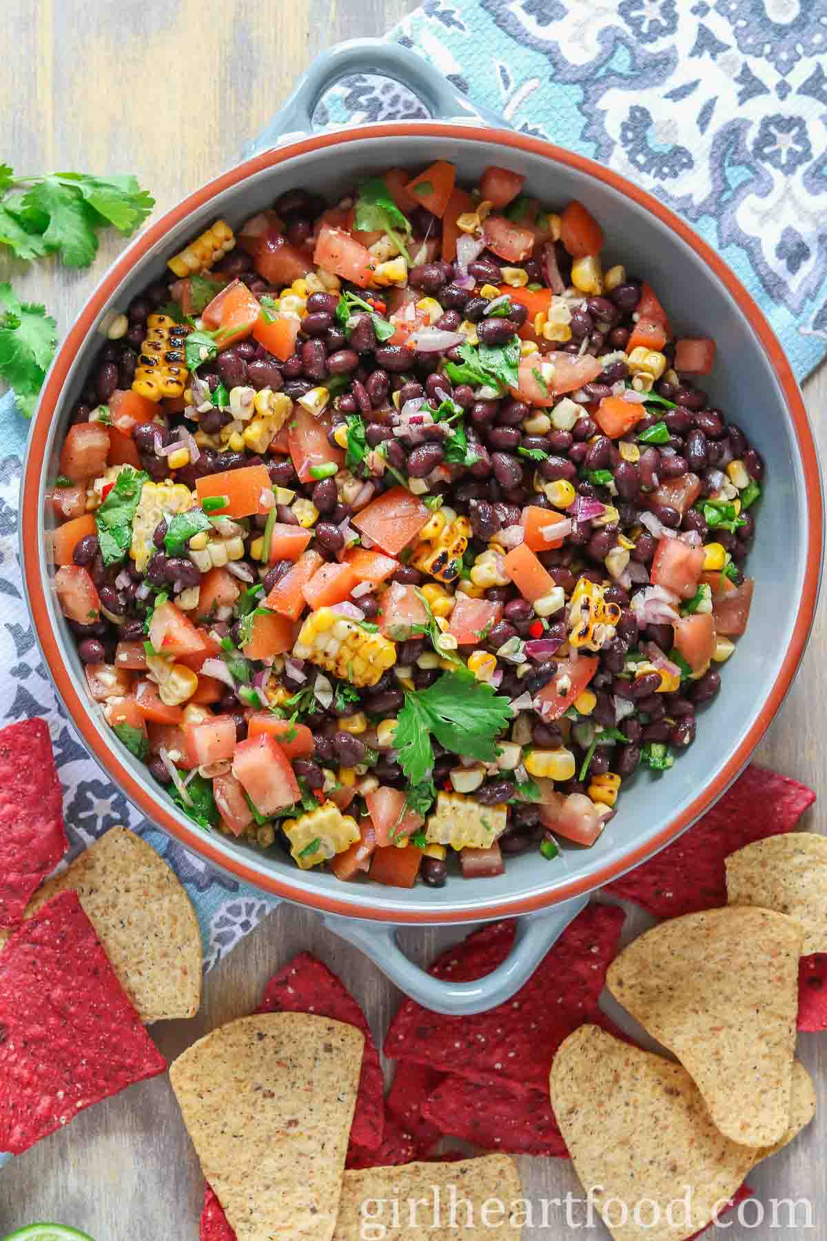 Dish of black bean and corn salsa, sitting on a tea towel, next to some tortilla chips.