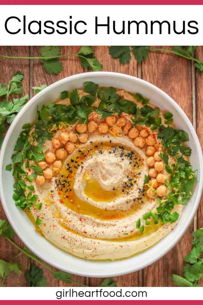 Bowl of hummus garnished with toppings and surrounded by fresh cilantro.