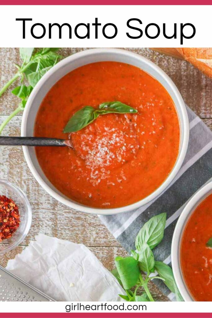 Bowl of tomato soup next to dish of red pepper flakes and basil.