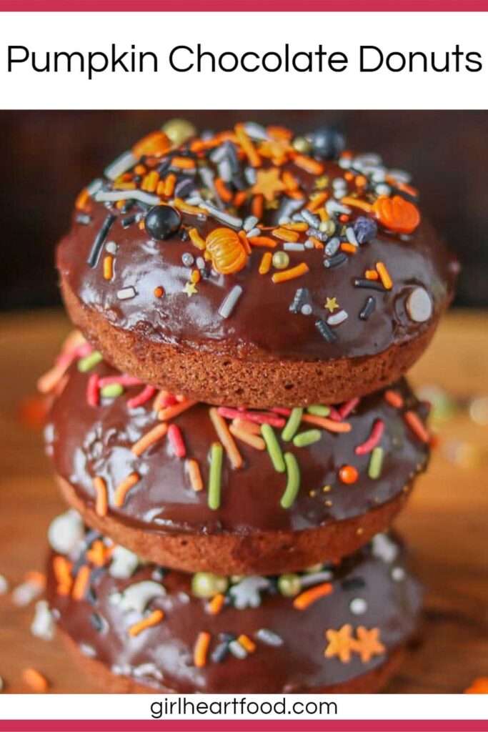 Stack of three pumpkin chocolate donuts with ganache and sprinkles.