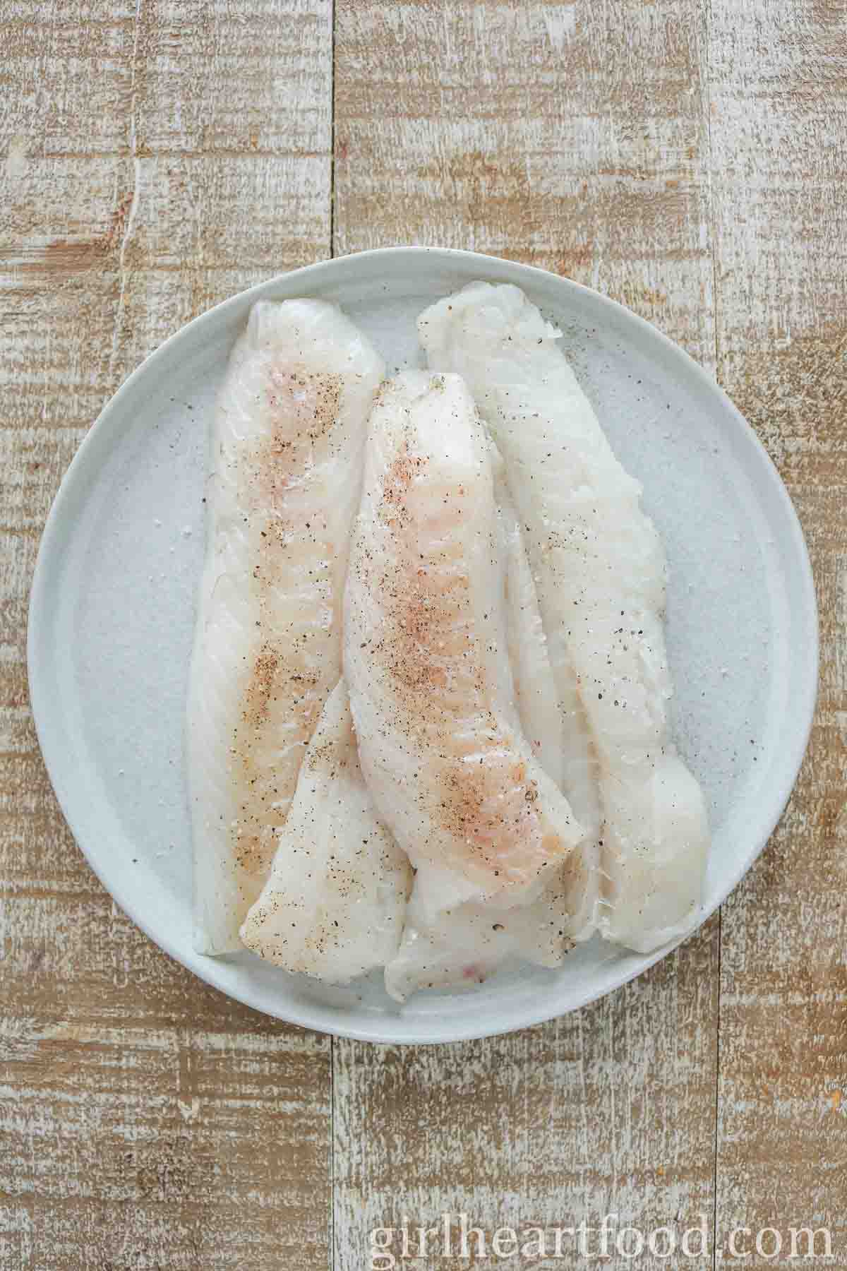 Uncooked, seasoned cod fillets on a light grey plate.