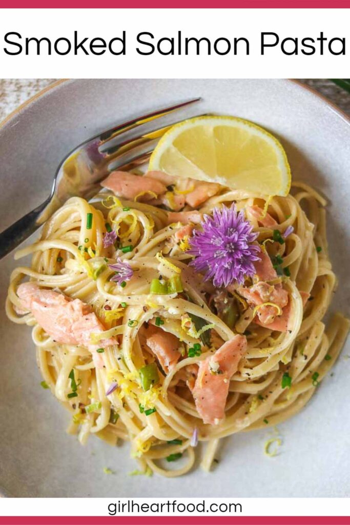 Bowl of creamy smoked salmon pasta garnished with lemon zest and chive flowers.