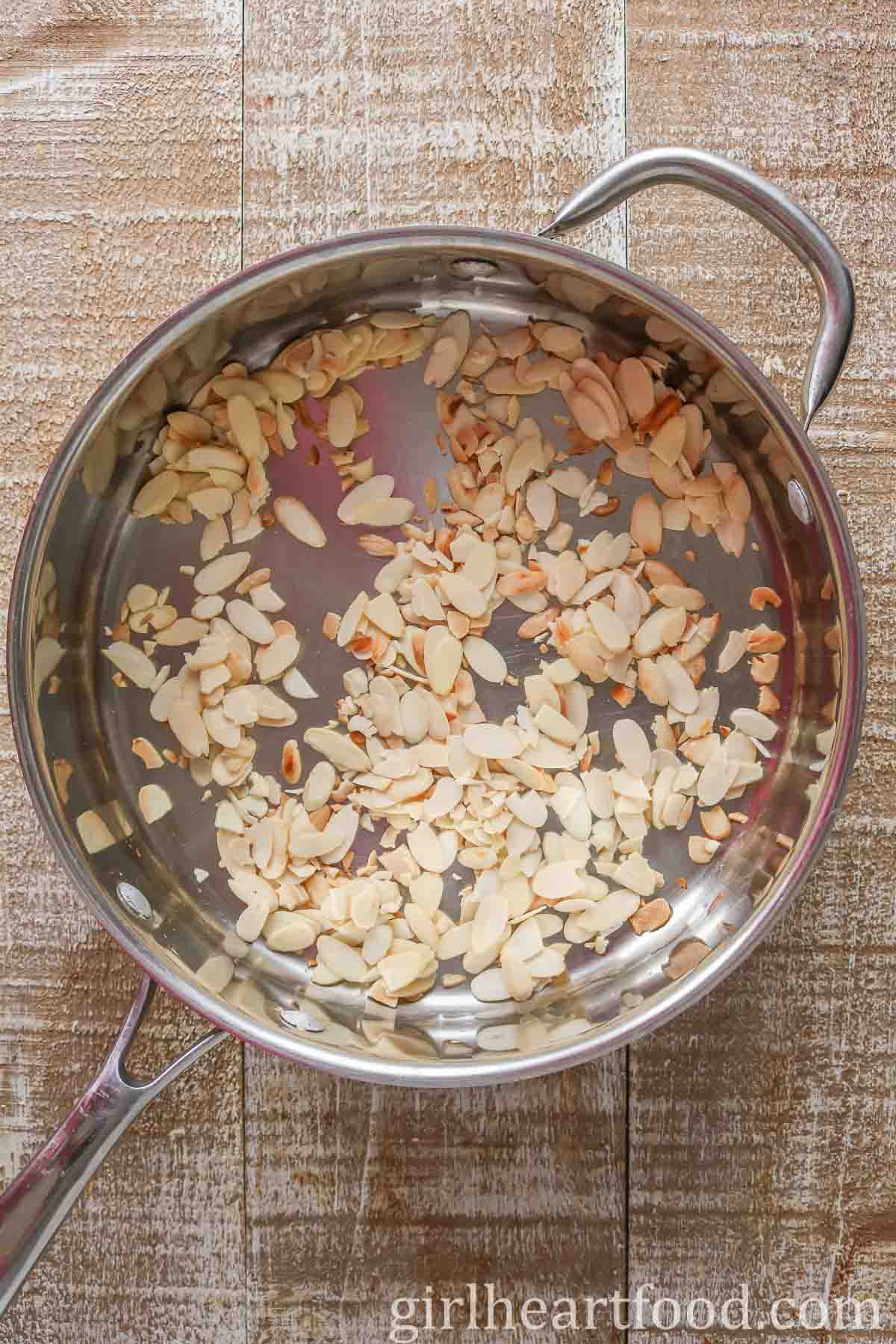 Sliced, toasted almonds in a stainless steel pan.