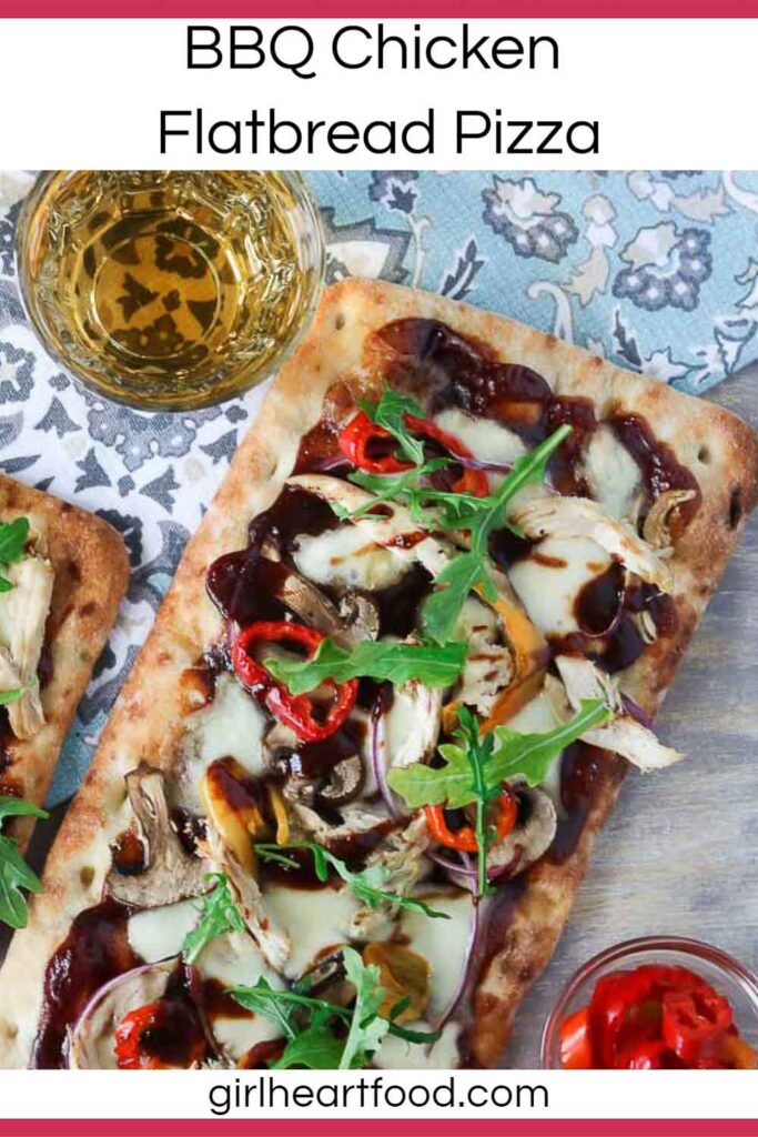 BBQ chicken flatbread pizza next to a glass of wine and dish of hot peppers.