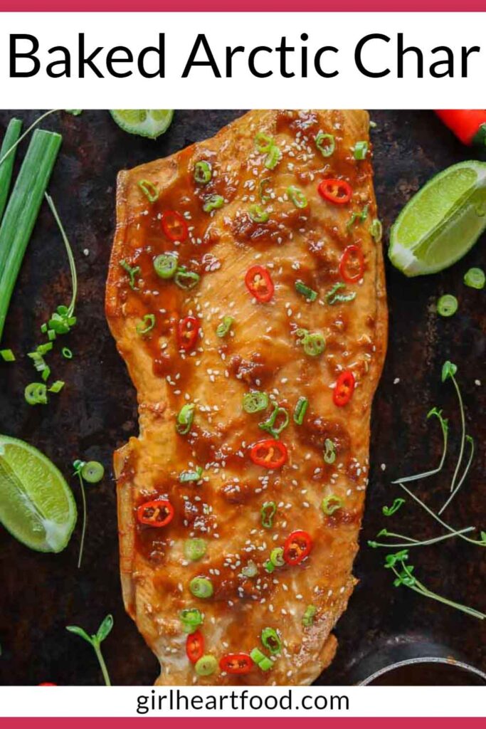 Fillet of cooked arctic char on a sheet pan topped with chili pepper, sesame seeds & green onion.
