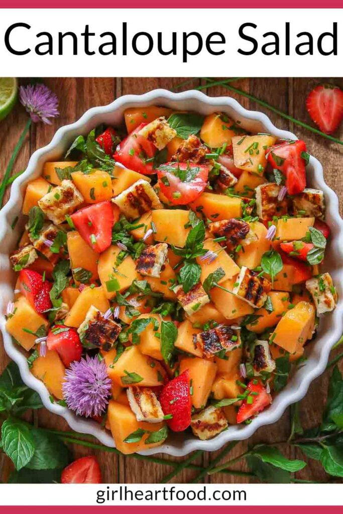 Cantaloupe salad in a bowl surrounded by fresh herbs, lime and berries.