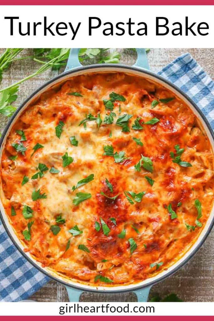 Cheesy turkey pasta bake in a pan garnished with parsley.