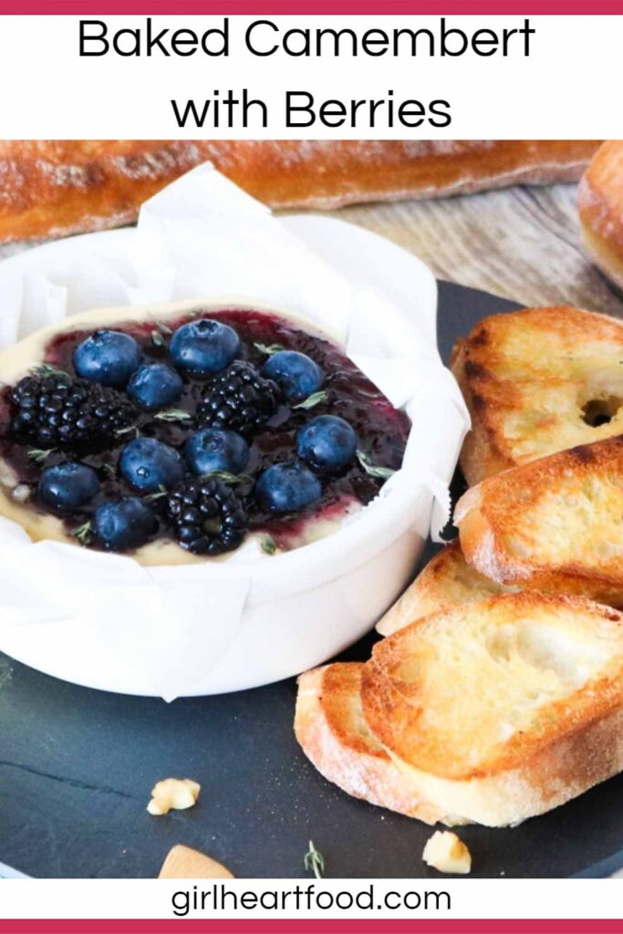 White dish of baked camembert with berries alongside some bread.