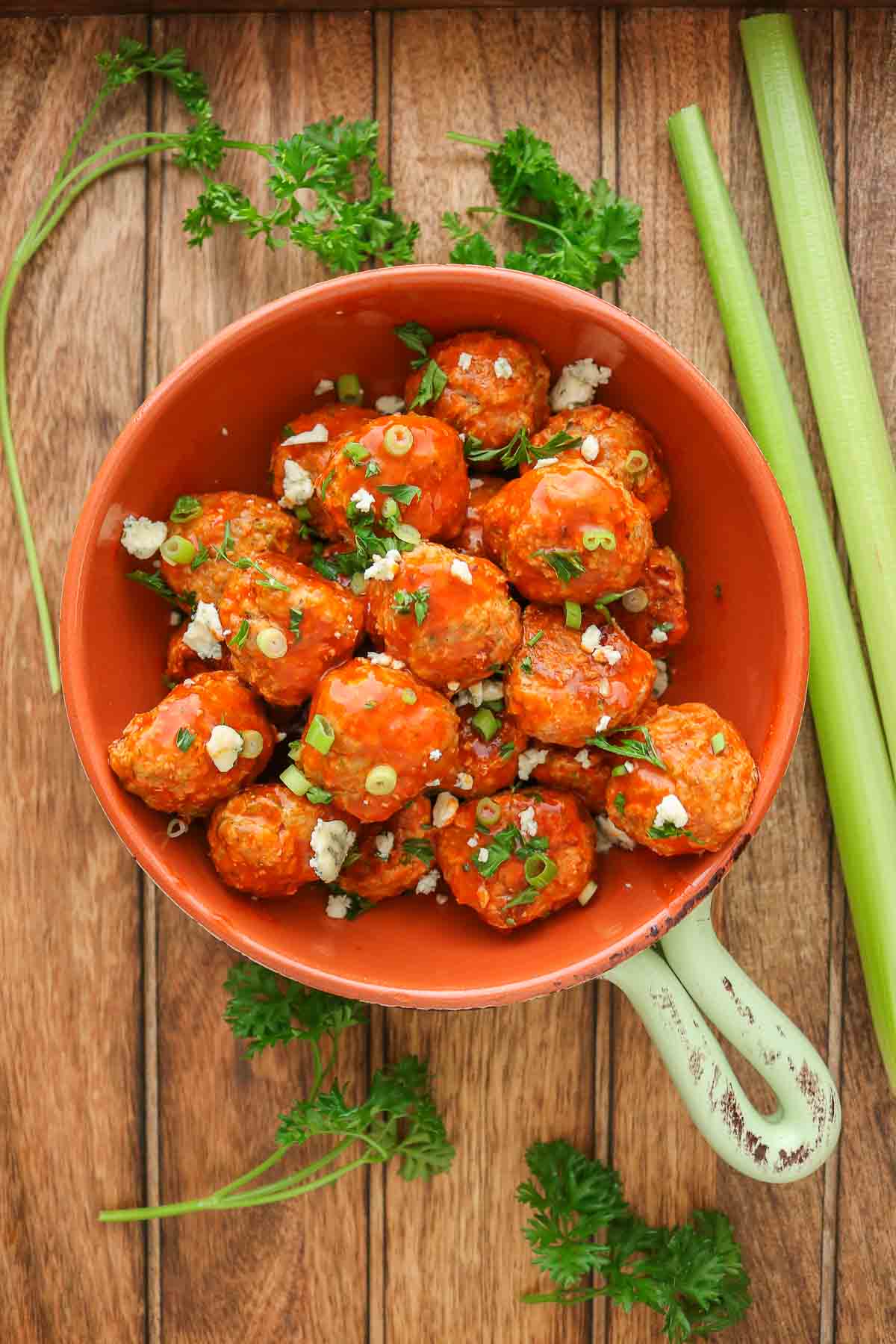 Buffalo turkey meatballs in a serving dish garnished with parsley, green onion and blue cheese.