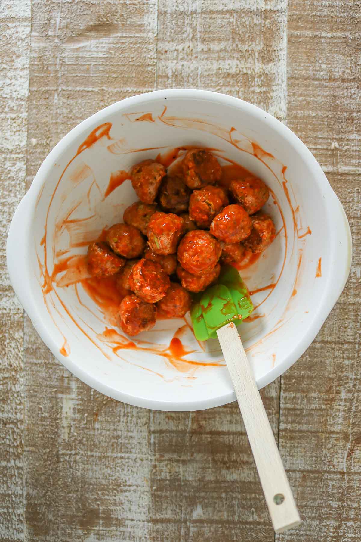 Stirring together turkey meatballs and buffalo sauce in a bowl with a rubber spatula.