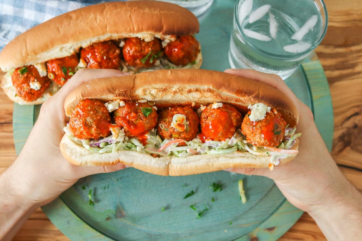 Two hands holding a buffalo turkey meatball sandwich.