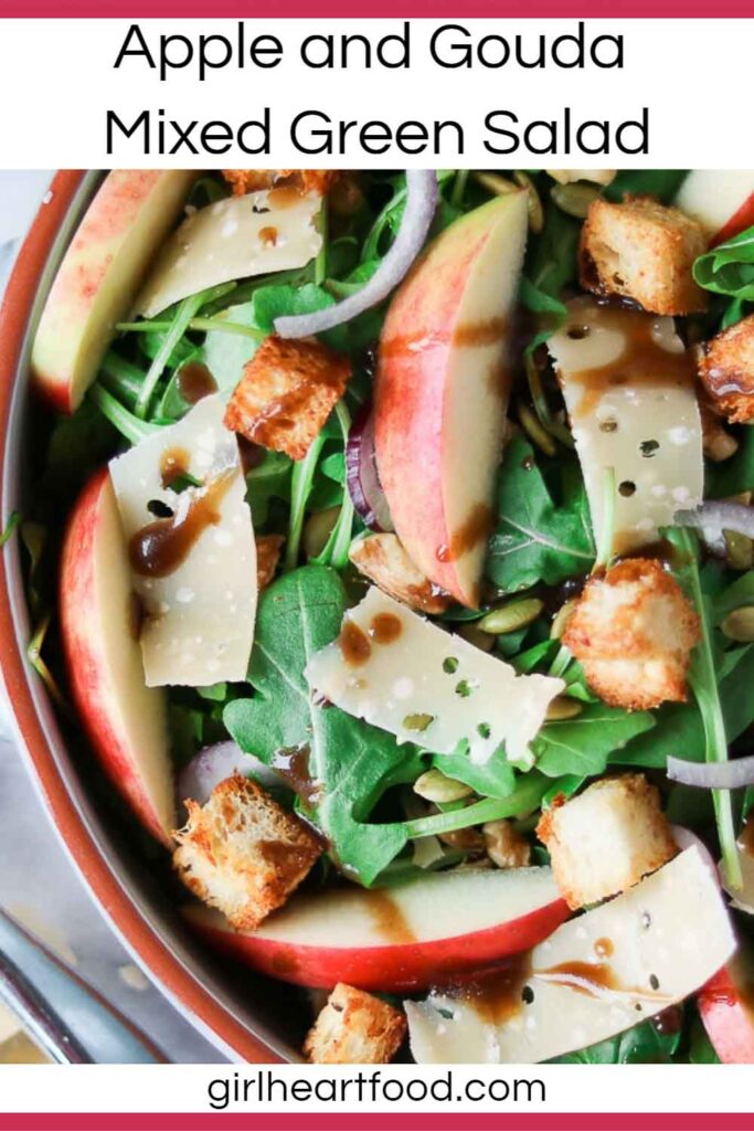 Close-up of a mixed green salad with cheese, apple, onion, croutons and vinaigrette.