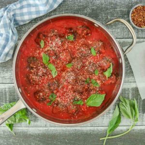 Pan of baked meatballs in tomato sauce garnished with basil and Parmesan.