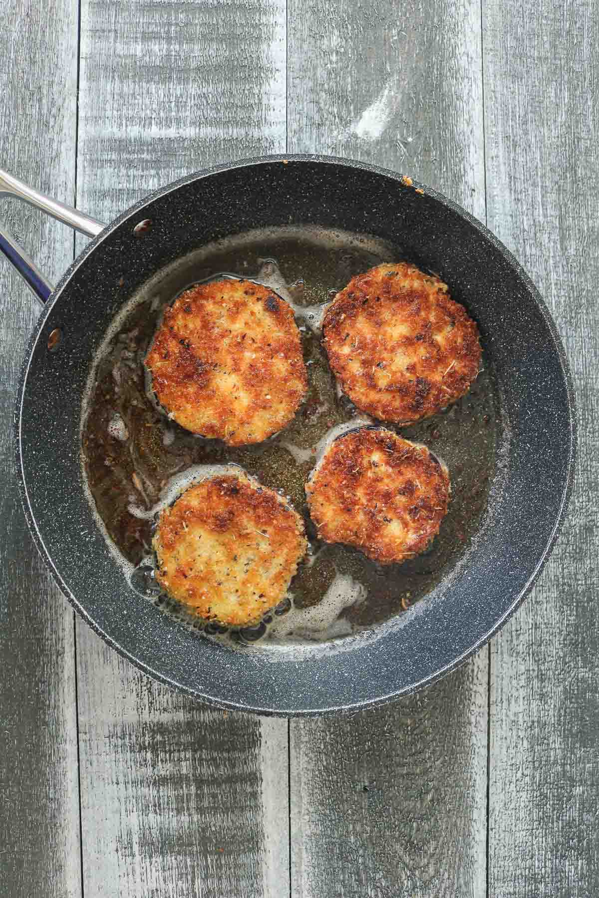 Four crispy breaded eggplant slices frying in a pan.