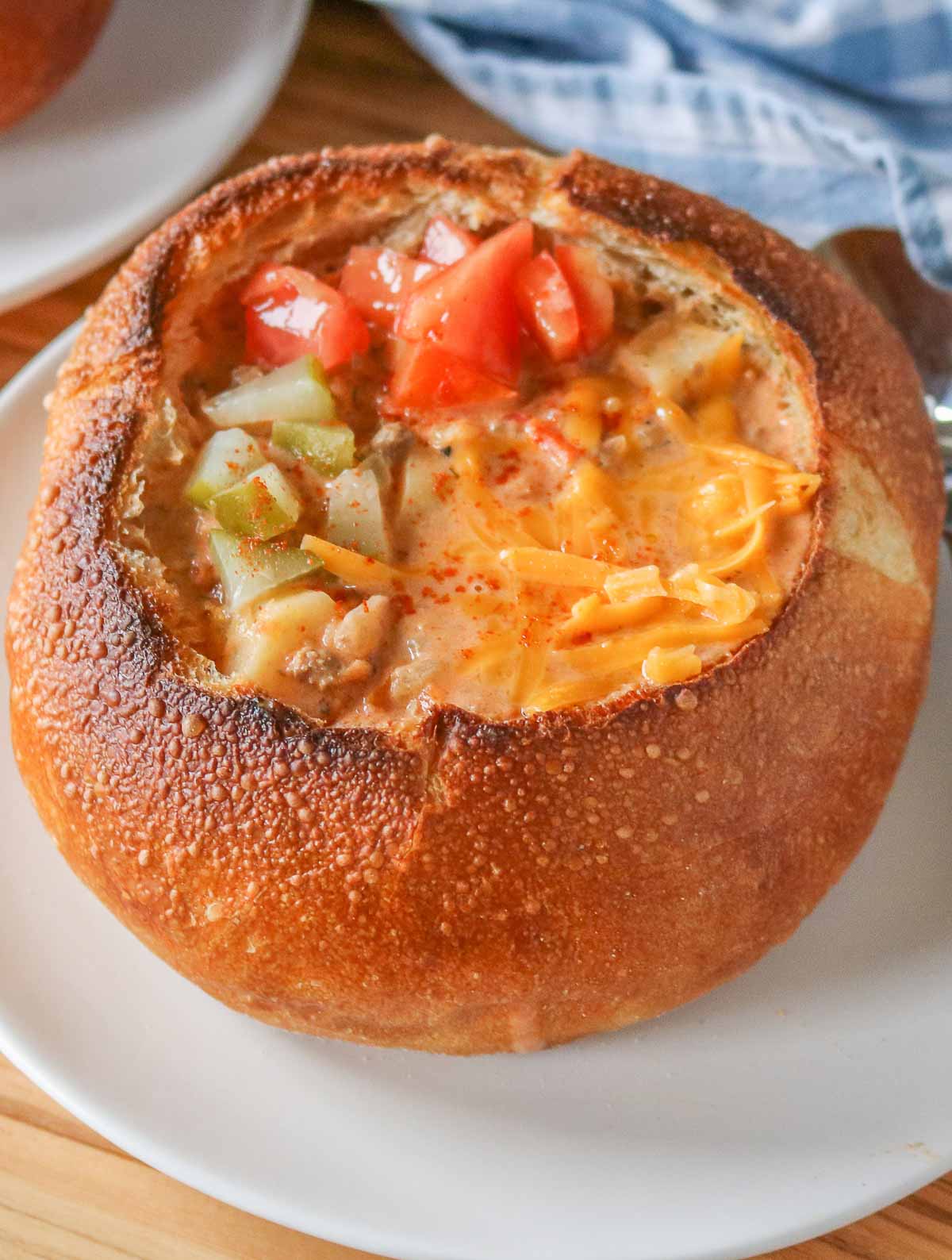 Cheeseburger soup in a bread bowl garnished with pickles, tomatoes and cheese.