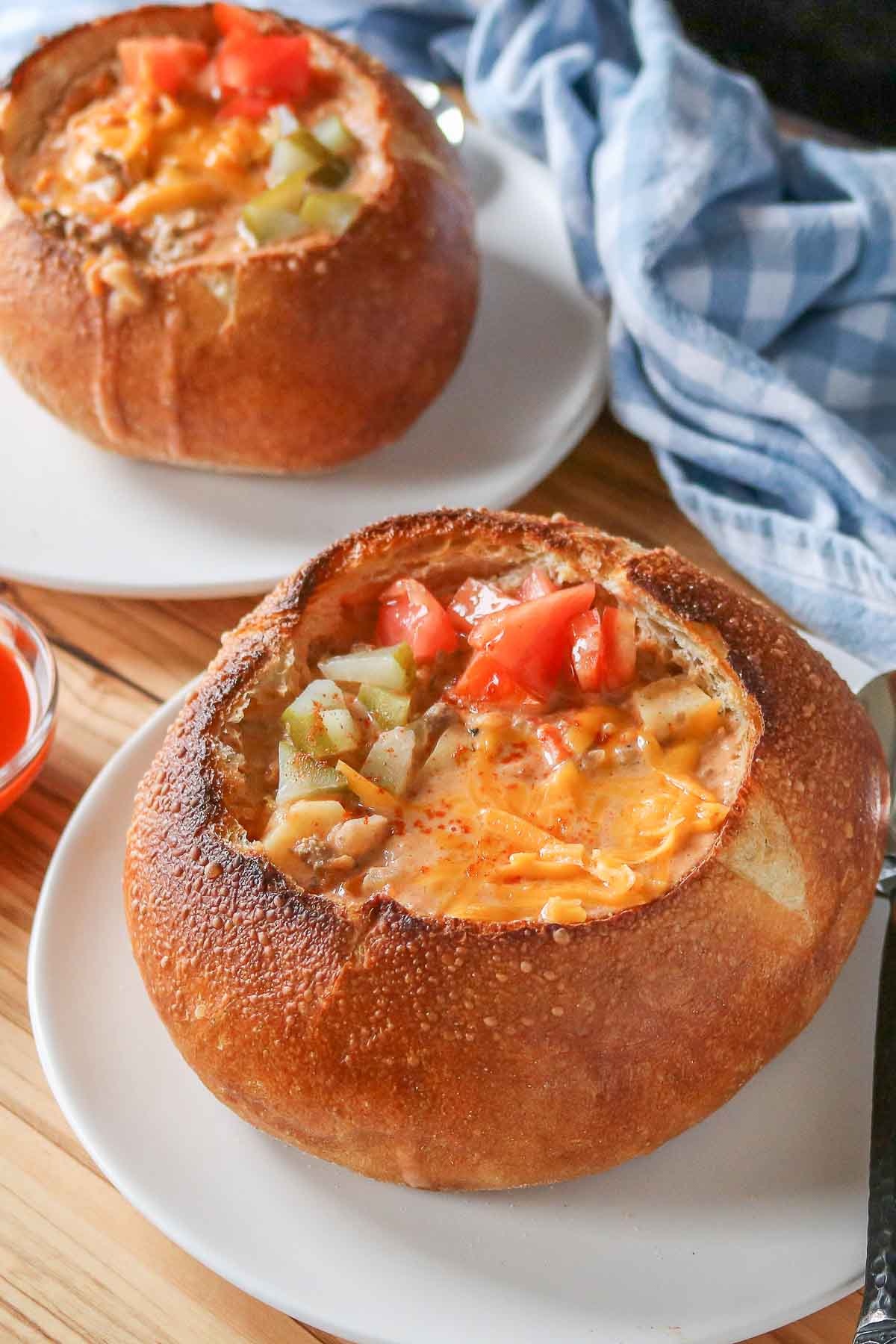 Two bowls of cheeseburger soup in a bread bowl, each garnished with toppings.