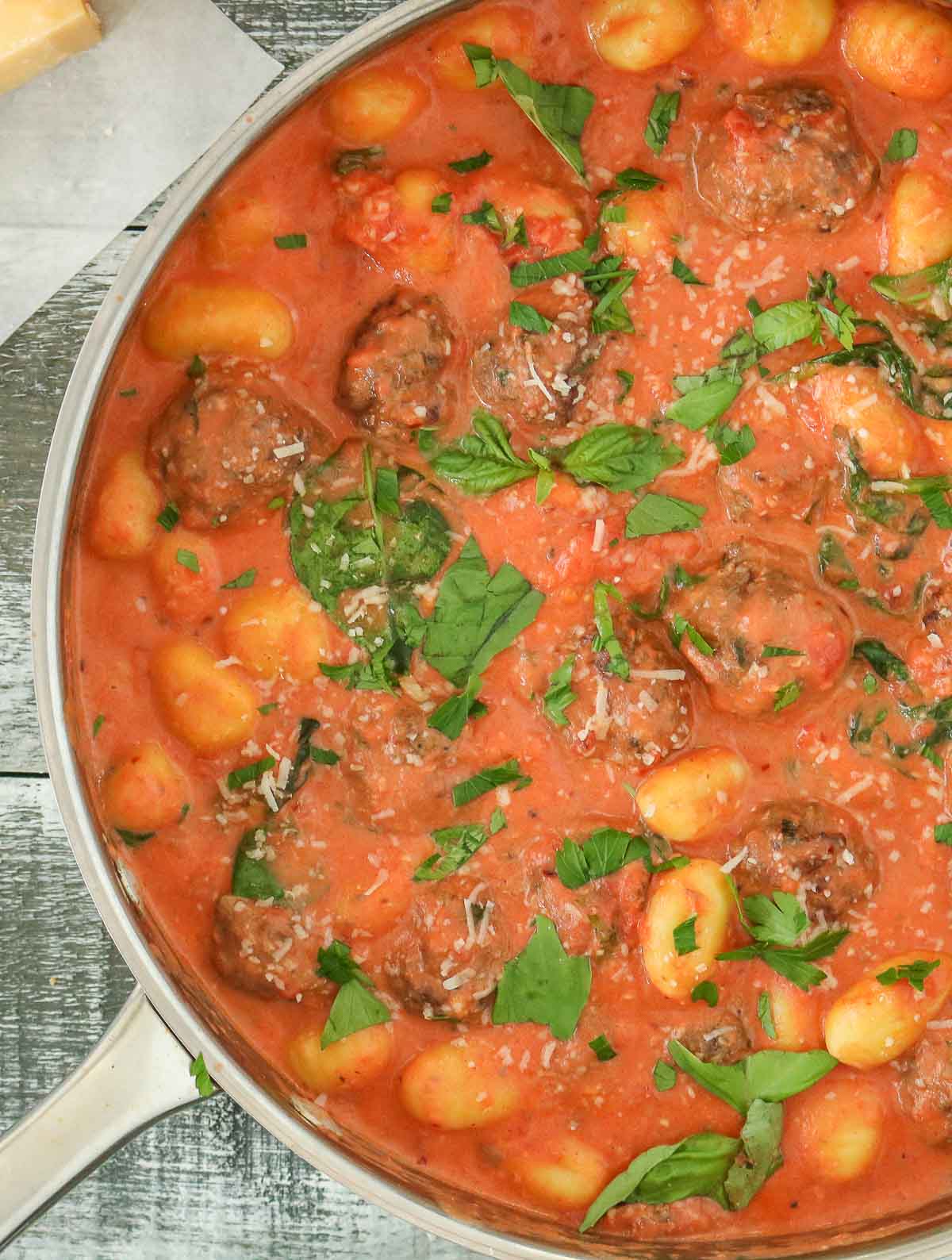 Close-up of a pan of gnocchi and meatballs in sauce garnished with basil and Parmesan.