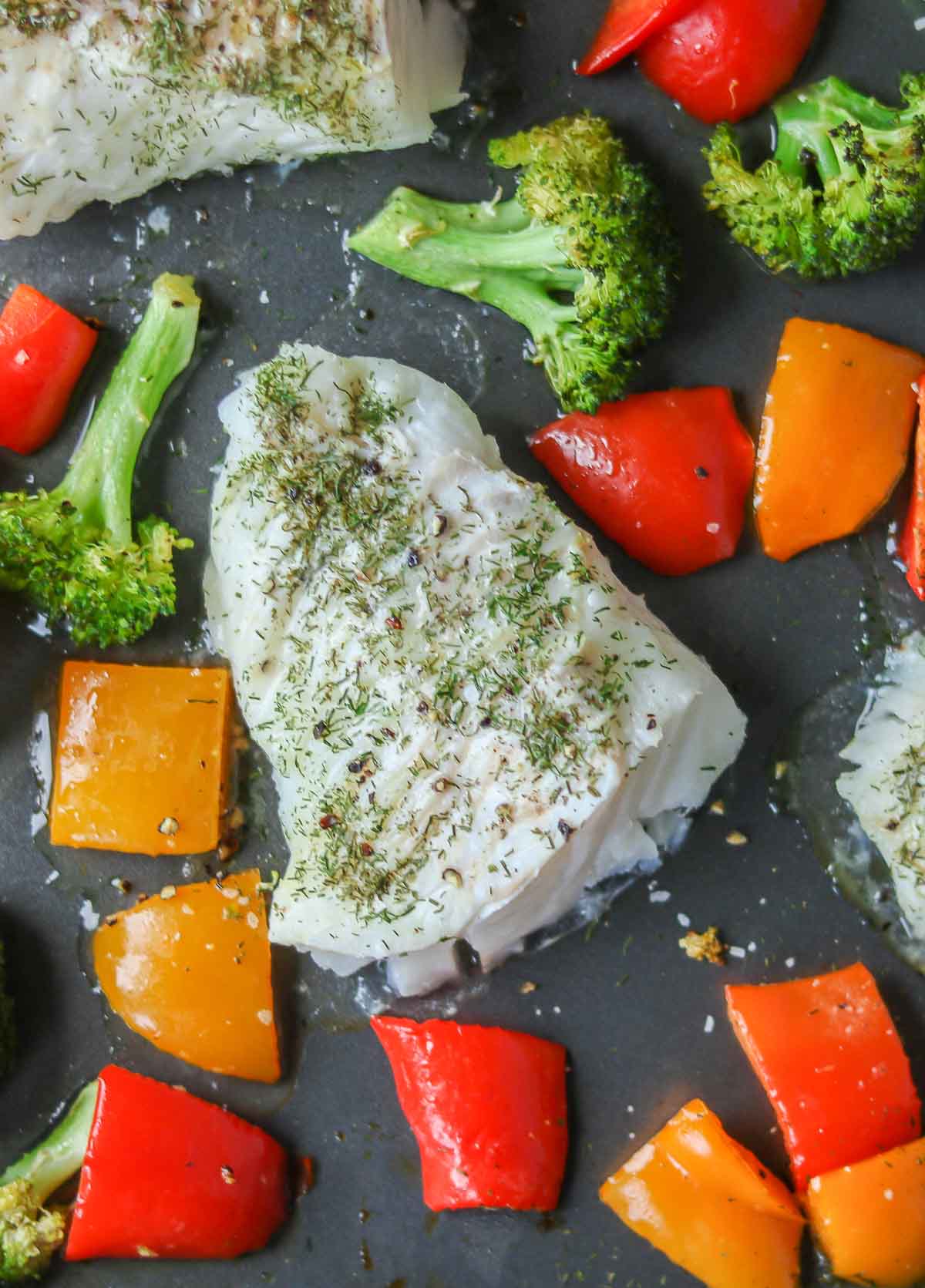 Portions of oven-baked cod and vegetables on a sheet pan.