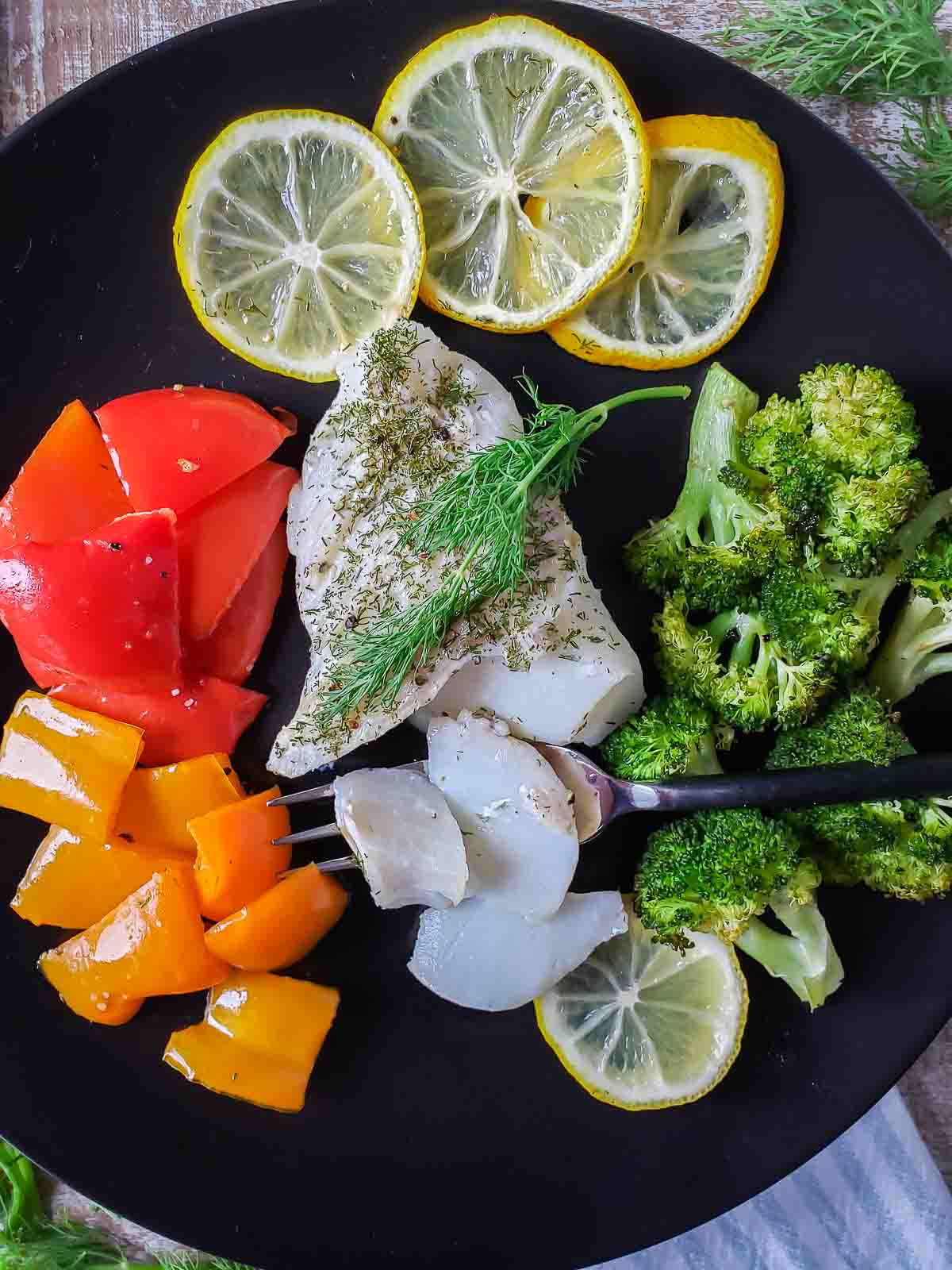 Portion of cooked cod, veggies and lemon slices on a plate.
