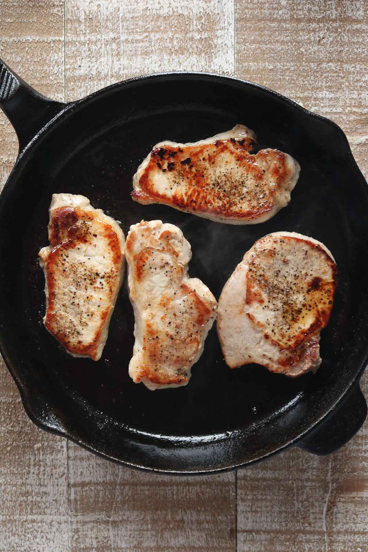 Four boneless pork chops in a cast-iron-pan.