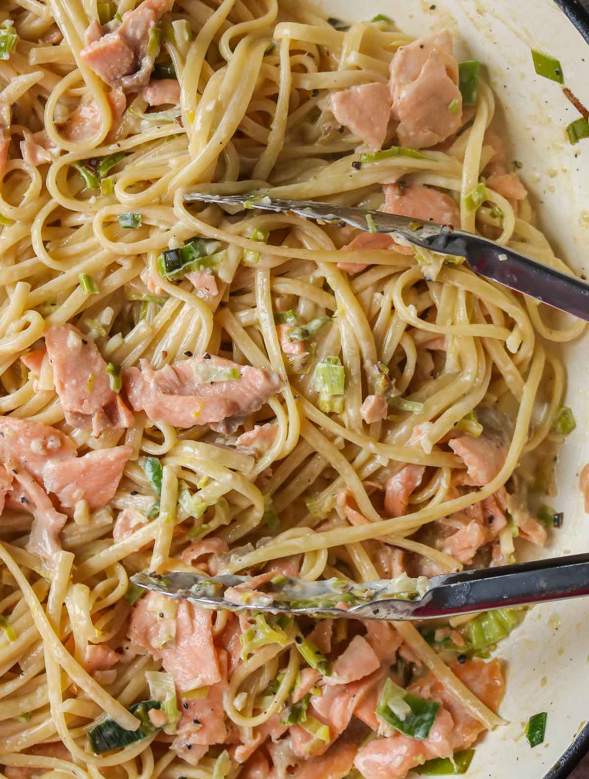 Pot of creamy smoked salmon pasta with a pair of tongs resting on top.