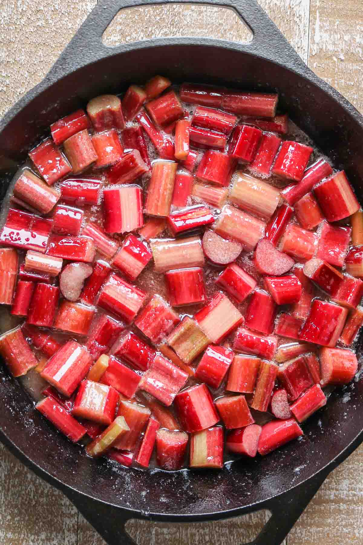 Chunks of rhubarb being coated in a sugar mixture in a cast-iron-skillet.