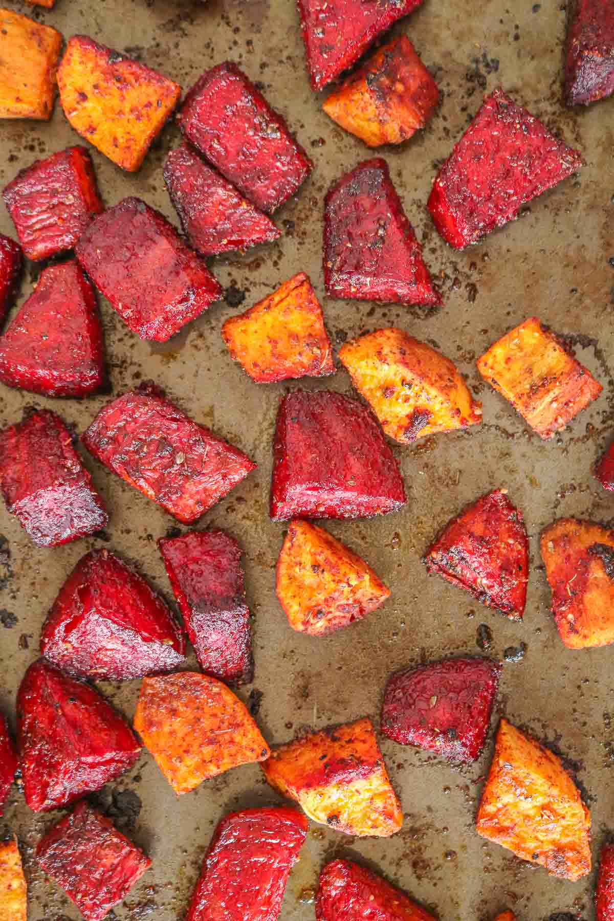 Chunks of roasted beets and sweet potatoes on a sheet pan.