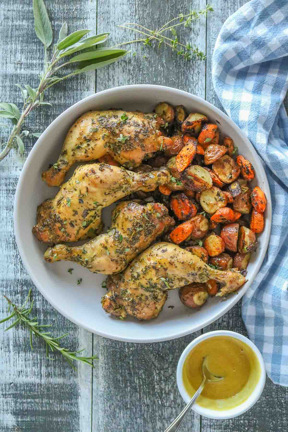 Roasted chicken legs and veggies in a serving dish, next to dish of honey mustard sauce.