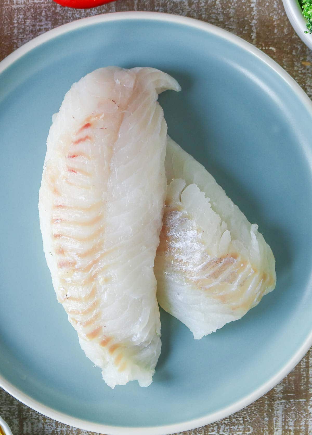 Two large uncooked cod fillets on a blue plate.