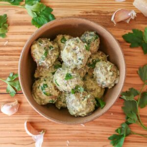 Chicken meatballs with pesto cream sauce in a bowl garnished with parsley and Parmesan.