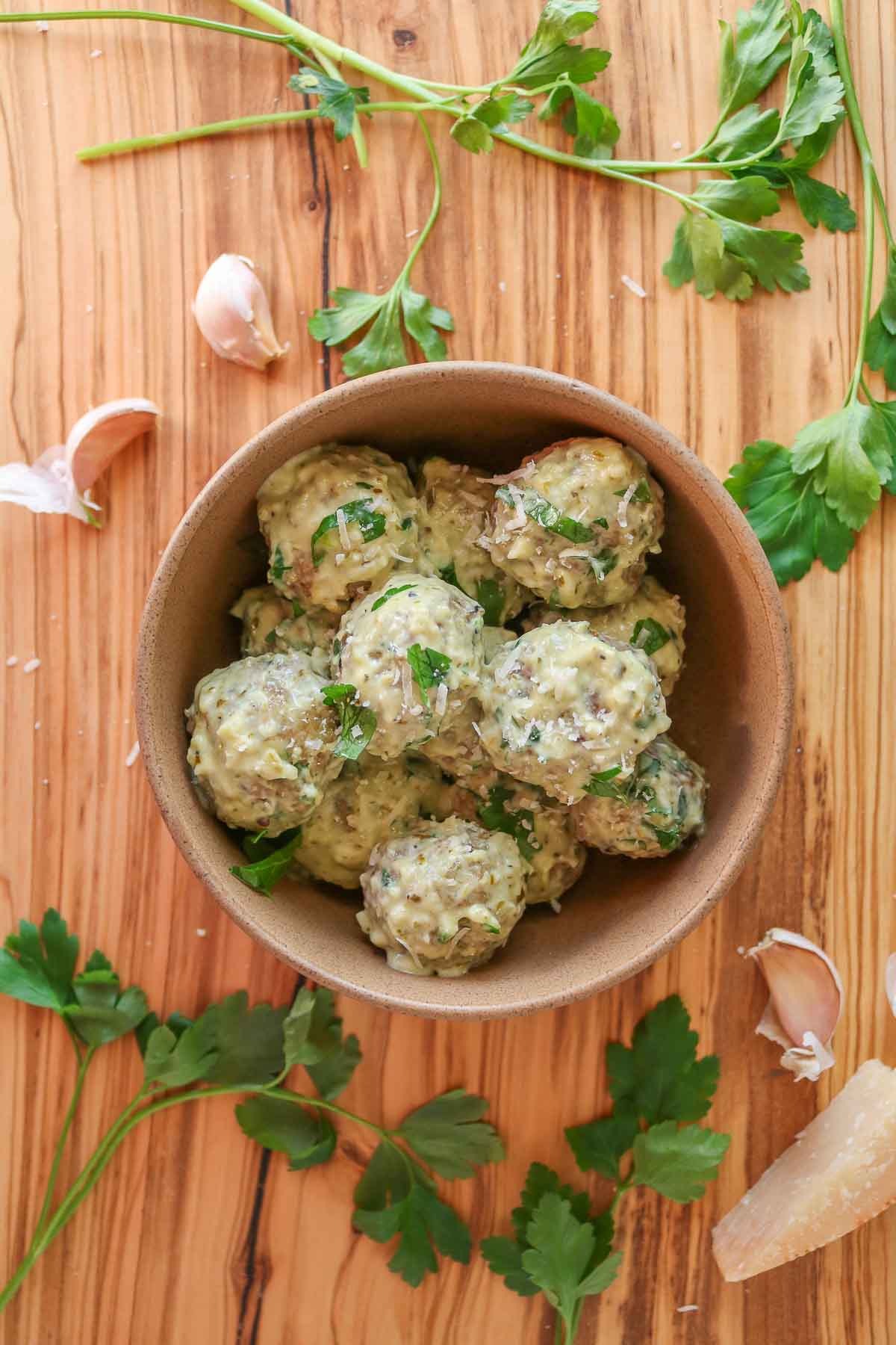 Chicken meatballs with pesto cream sauce in a bowl garnished with parsley and Parmesan.