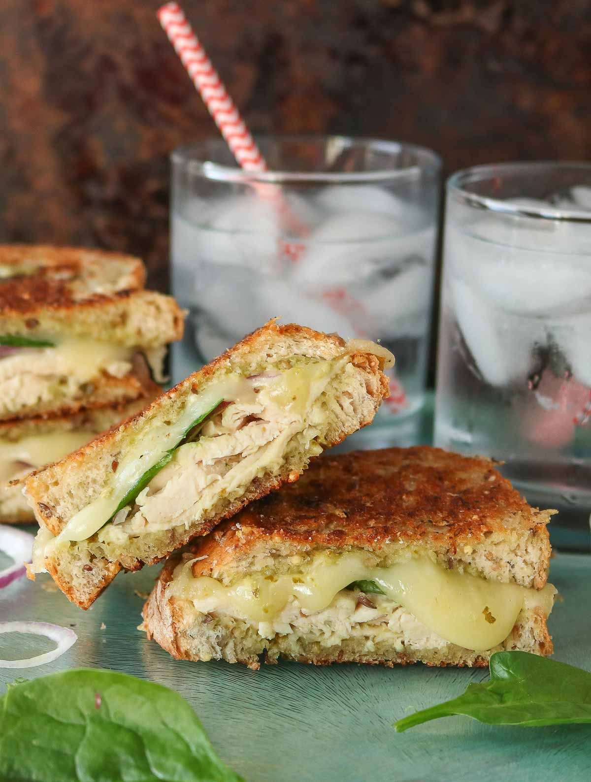 Two halves of a chicken pesto grilled cheese sandwich, one half resting on the other half.