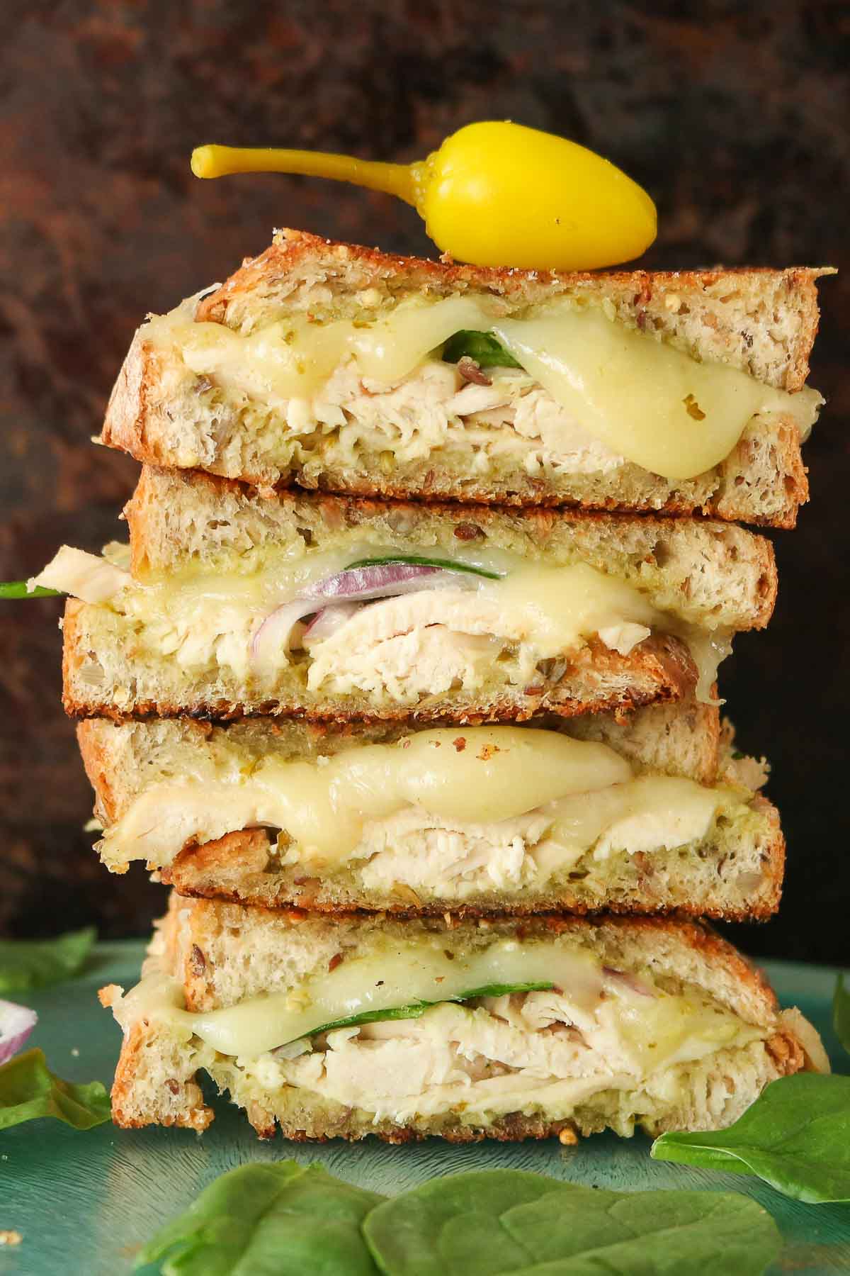 Stack of four chicken pesto grilled cheese sandwich halves with a hot pepper on top.