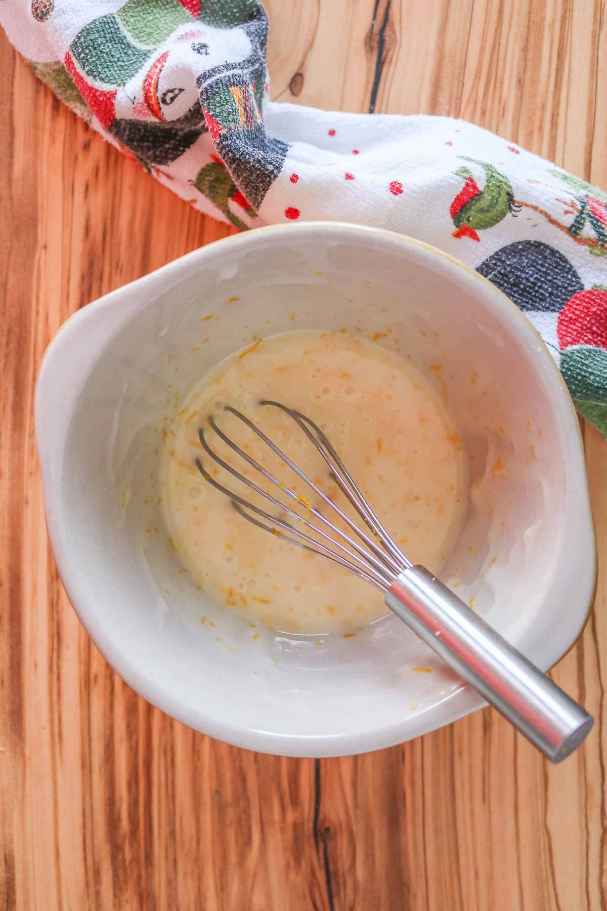 Orange icing sugar glaze in a bowl with a whisk resting in the bowl.