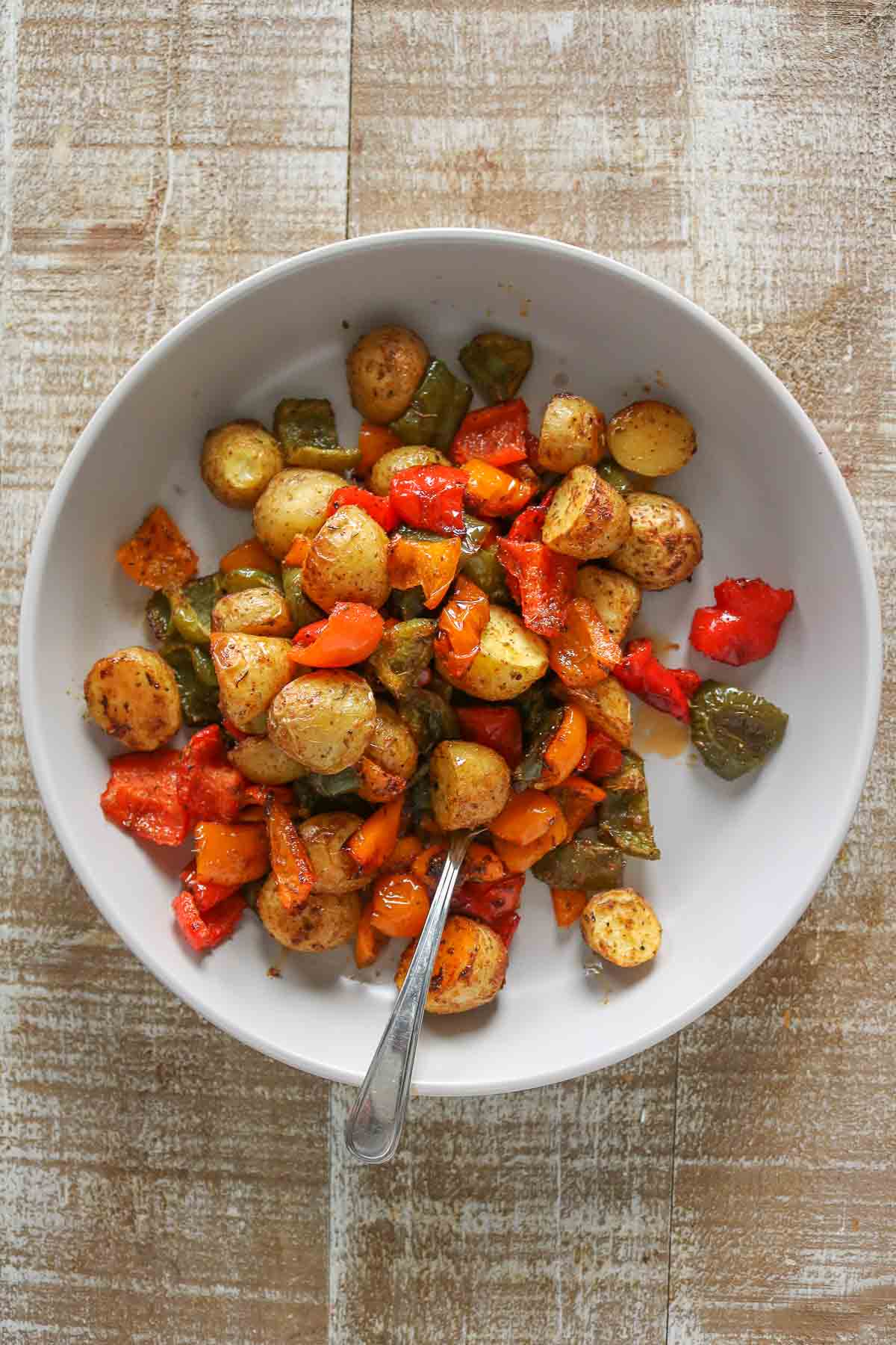 Roasted potatoes and bell peppers in a serving dish with a spoon resting in it.