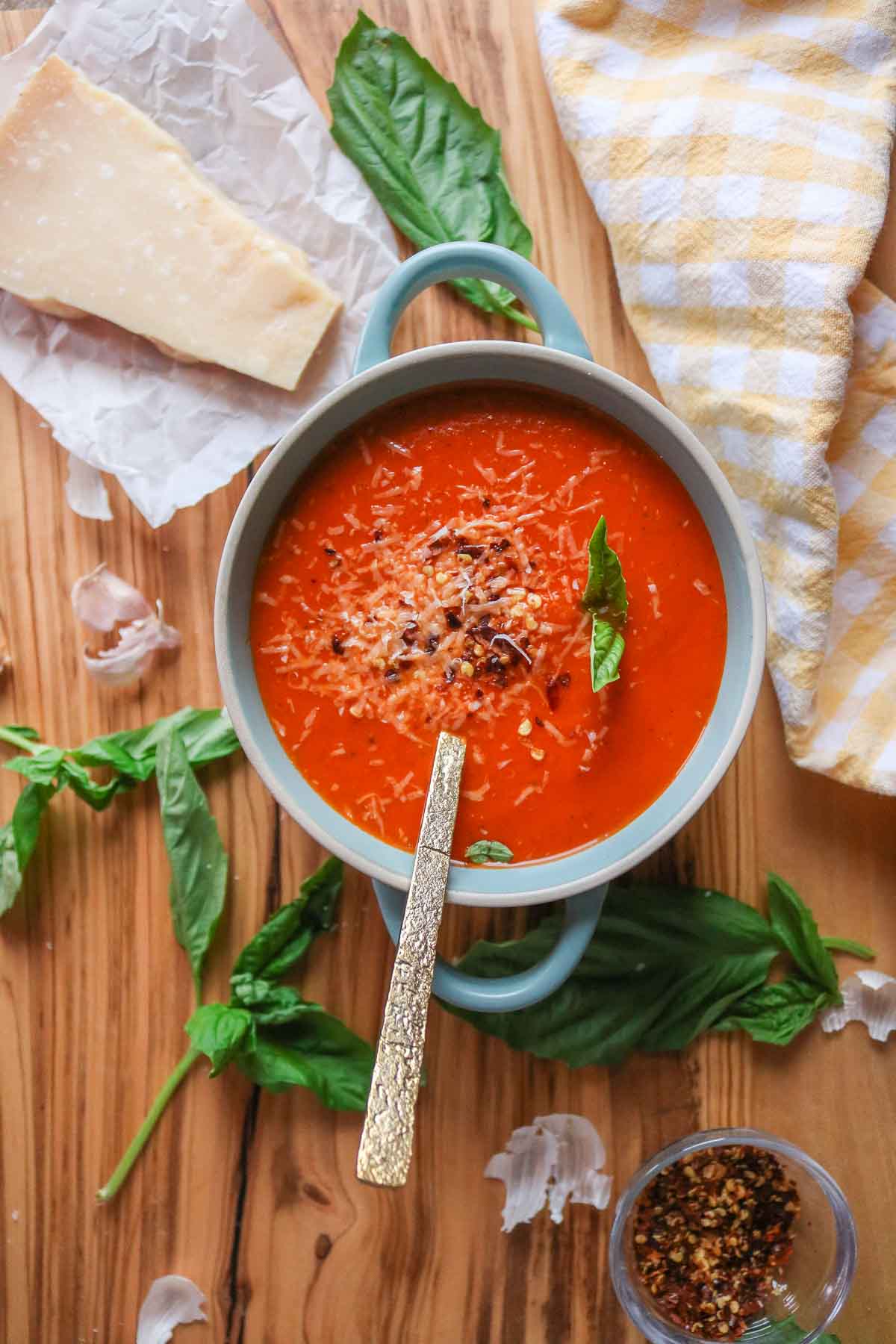 Bowl of creamy tomato basil soup garnished with cheese, red pepper flakes and basil.